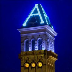 a clock tower lit up at night with blue lights on it's sides and the letters a above them