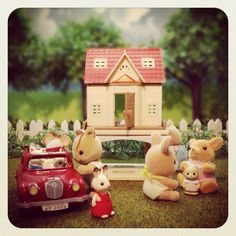 a group of stuffed animals sitting in front of a toy house with a car parked next to it