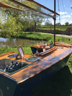 an old fashioned boat with drinks on it is parked in the grass next to a body of water