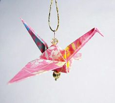 a pink origami bird hanging from a gold chain on a white sky background