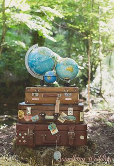 three suitcases stacked on top of each other in the woods with an earth globe on top