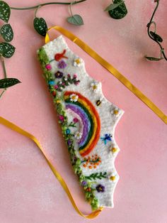 a piece of cake decorated with rainbows and flowers on a pink surface next to green leaves