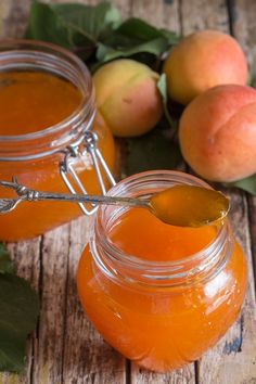 two jars filled with liquid sitting on top of a wooden table next to peaches