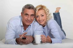 a man and woman laying on top of a bed next to each other holding coffee mugs