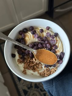 a bowl filled with granola and blueberries on top of a table next to a person holding a spoon