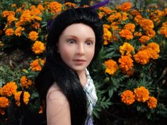 a doll with long black hair standing in front of flowers