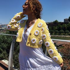 a woman in a white dress and yellow cardigan is standing on a balcony with her hands to her face