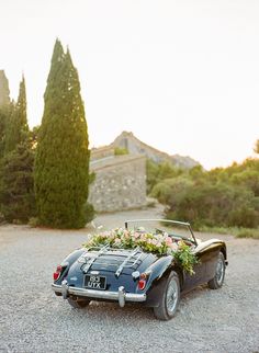 an old black sports car with flowers in the back