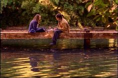 two people are sitting on a pier in the water