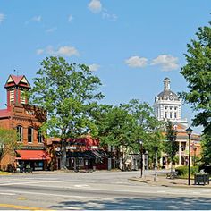 an empty street with buildings and trees on both sides in front of a clock tower