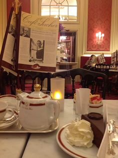 a table topped with plates and cups filled with cake next to a sign that says cafe de paris