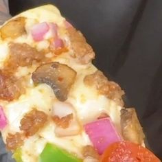 a close up of a person holding a slice of pizza with toppings on it