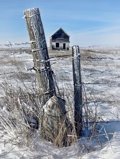 an old shack sits in the middle of a snowy field next to a barbed wire fence