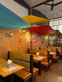 an empty restaurant with wooden tables and benches under colorful umbrellas hanging from the ceiling