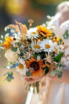 a woman holding a bouquet of white and yellow flowers with greenery in her hands