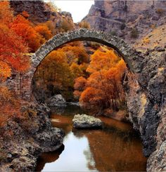 an old stone bridge over a river surrounded by autumn colored trees in the mountainside