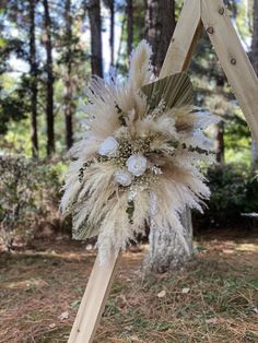 a wooden easel with flowers and feathers on it in the grass next to trees