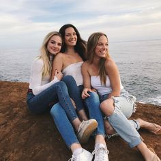 three young women sitting on the beach with their arms around each other