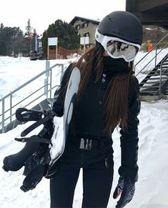 a woman standing in the snow with her skis and goggles strapped to her chest