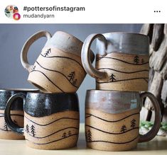 four coffee mugs are stacked on top of each other, with mountains and trees painted on them