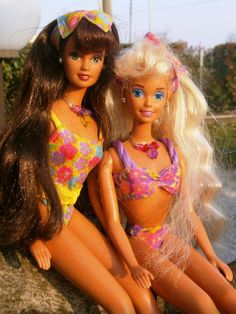 two barbie dolls sitting next to each other on a rock in front of a body of water