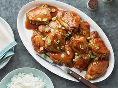 a white plate topped with chicken covered in sauce and rice next to two bowls filled with rice