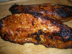 two pieces of grilled meat sitting on top of a wooden cutting board next to each other