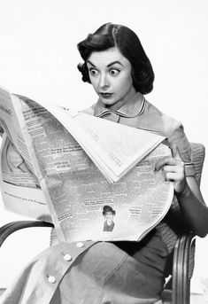 a black and white photo of a woman reading a newspaper