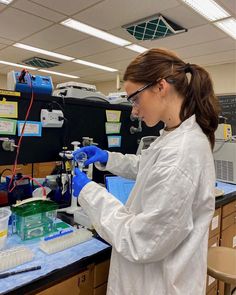 a woman in white lab coat and goggles working on a pipe with blue liquid