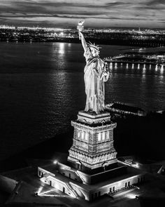 the statue of liberty is lit up at night in black and white, with city lights behind it