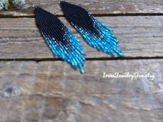 two blue and black beaded earrings sitting on top of a wooden table next to flowers