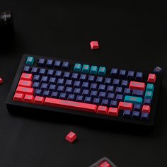 a red and blue computer keyboard sitting on top of a black table next to a cell phone