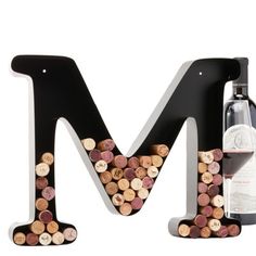 the letter m is made out of wine corks and sits next to a bottle of wine