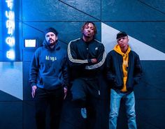 three young men standing next to each other in front of a blue and white wall