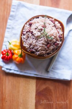 rice and beans in a brown bowl on a white napkin next to some tomatoes, peppers and a spoon