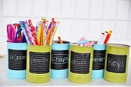 there are pencils and pens in tins on the counter next to each other