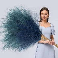 a woman in a blue dress holding a large bundle of long, feathery grass