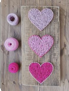 three hearts made out of yarn sitting on top of a wooden board next to two skeins of yarn