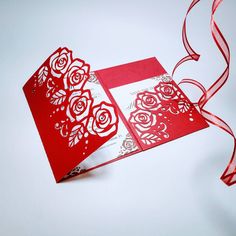 a red and white card with roses on it, next to a ribbon that has been cut into the shape of a heart