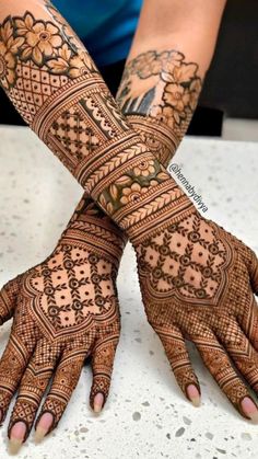 two hands with henna tattoos on them, one is showing the intricate design and the other has flowers