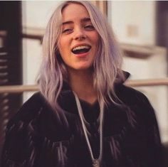 a woman with grey hair is smiling and wearing a black hoodie while standing in front of a building