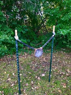 two metal poles with chains attached to them in the grass near some trees and bushes