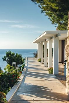 the walkway is lined with white pillars leading to an ocean side house and garden area