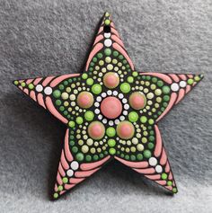 a pink and green star ornament on a gray surface with white dots in the center