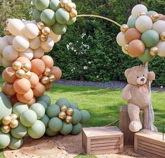 a teddy bear sitting on top of a wooden bench next to balloons in the shape of trees