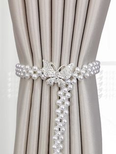 a white beaded bracelet with pearls and butterflies on the clasp, hanging from a curtain