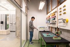 a man standing in front of a large printer on top of a green table next to a white wall