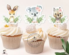 three cupcakes with frosting and animals on top, surrounded by greenery