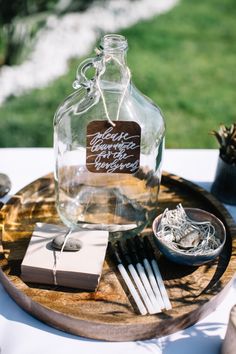 a wooden tray topped with a glass bottle filled with liquid next to a couple of silverware