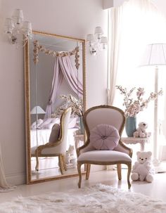 a white chair sitting in front of a mirror next to a teddy bear and vase with flowers